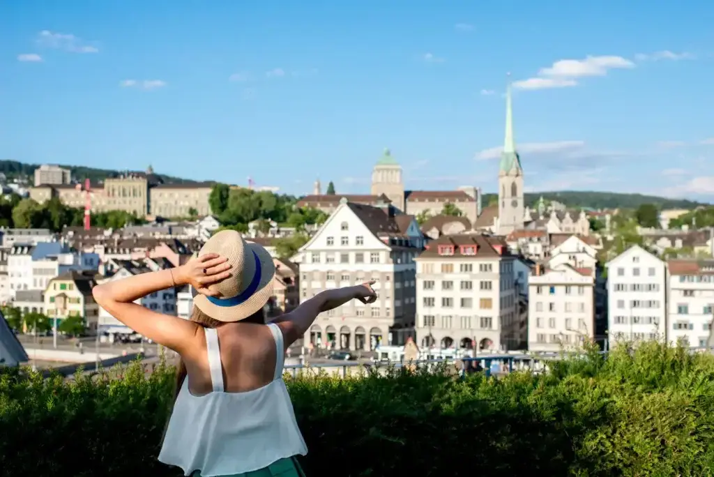 Woman in straw hat enjoying panoramic view of Zurich cityscape with iconic Grossmünster Church visible, perfect for Zurich travel inspiration.