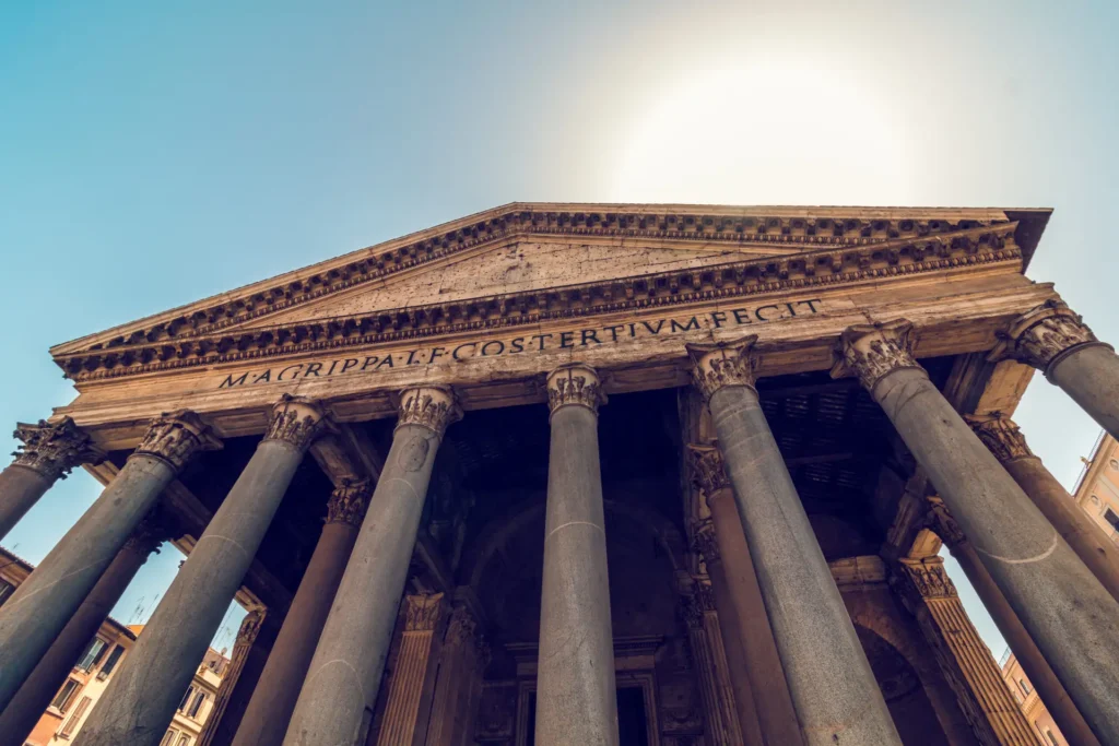 Low-angle view of the majestic Pantheon in Rome, showcasing ancient Roman architecture with detailed columns and inscriptions, under a clear sky.