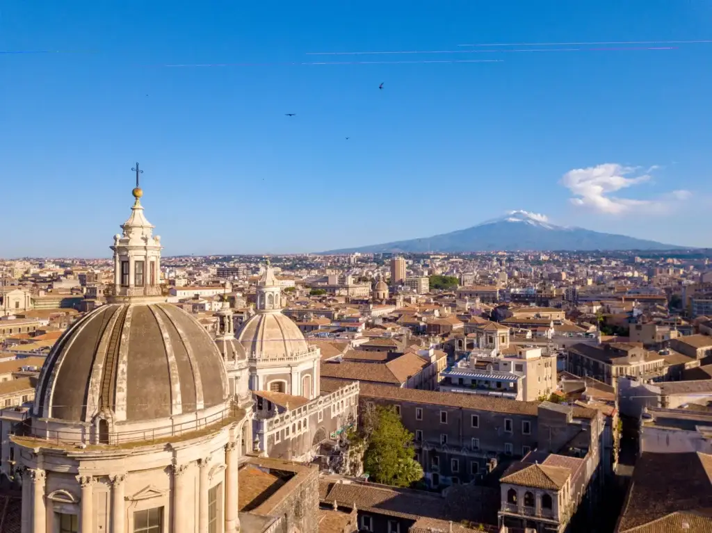Aerial view of the Cathedral of Sant'Agata in Catania, showcasing its stunning domes with Mount Etna in the background, epitomizing Sicilian heritage and architecture.