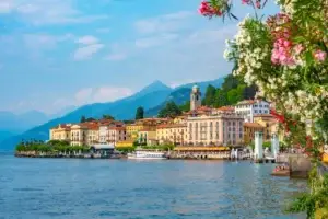 Scenic view of Bellagio, a picturesque town on Lake Como, Italy, showcasing vibrant architecture, a bustling waterfront with a boat, and lush floral foreground.