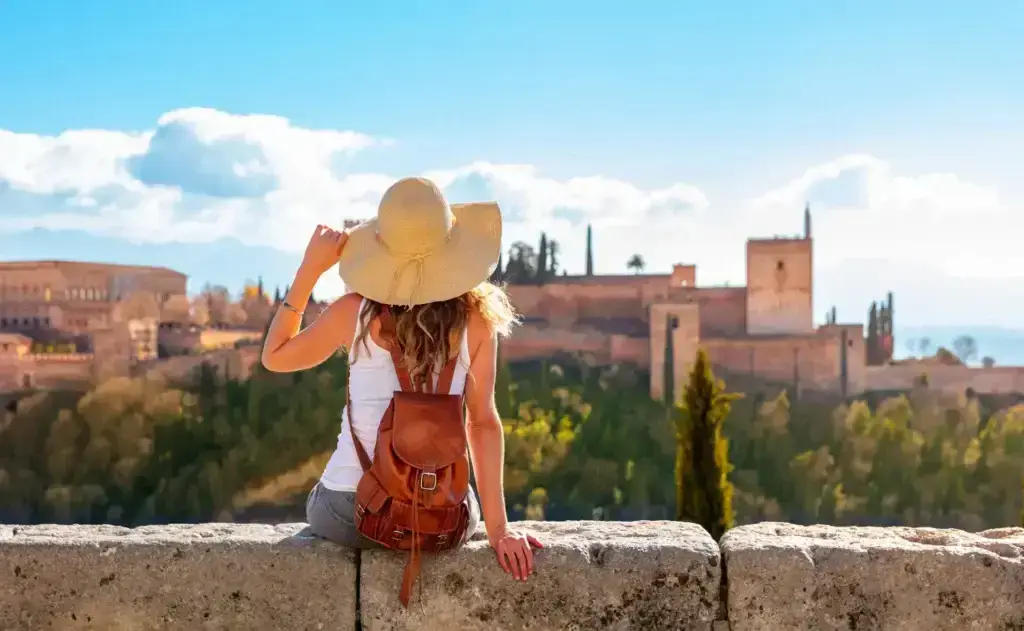 Woman in a straw hat admiring the Alhambra from a scenic overlook in Granada, Andalusia, emphasizing the rich cultural heritage and stunning architecture of Spain.