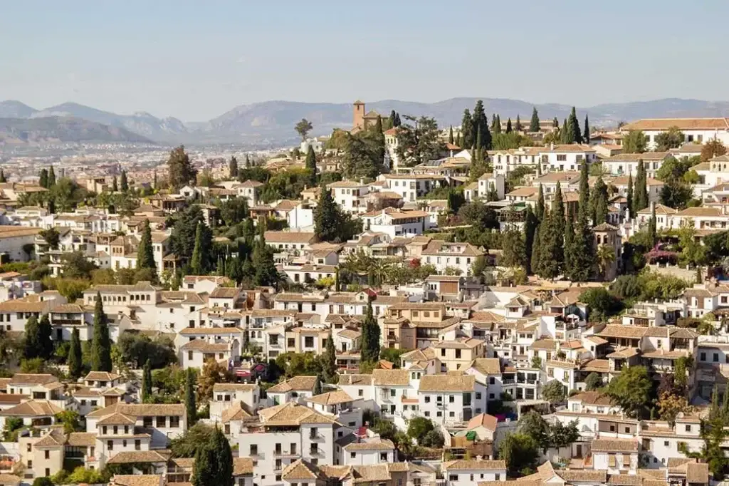 Panoramic view of the Albaicin district in Granada, showcasing traditional white houses and narrow winding streets against a backdrop of the Sierra Nevada mountains.