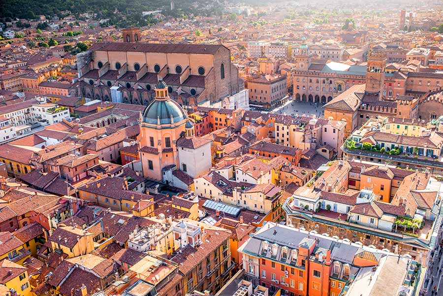 Aerial view of Bologna, Italy featuring historic architecture with the prominent San Petronio Basilica and terracotta rooftops under a soft golden light.
