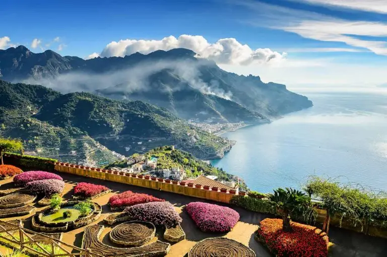 Breathtaking view of Ravello, Italy, showcasing vibrant floral gardens and the expansive Amalfi coast under a clear blue sky.