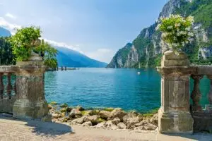 Scenic view of Lake Garda, Italy with mountains in the background and a flower-adorned stone balustrade in the foreground.