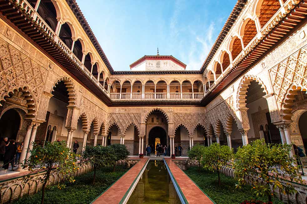 Courtyard of the Real Alcazar in Seville, Spain showcasing Moorish architecture, ornamental craftsmanship, and a serene water feature.