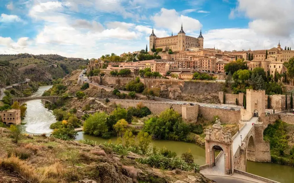 Panoramic view of Toledo, Spain featuring the historic Alcázar and Tagus River with medieval bridge