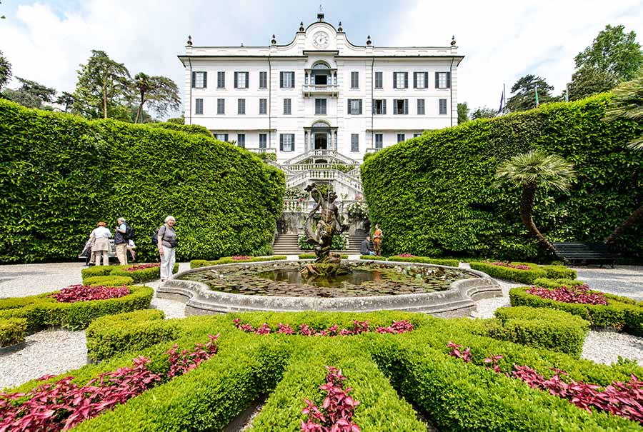 Visitors exploring the beautifully manicured gardens of Villa Carlotta on Lake Como, Italy, featuring vibrant flower beds and classical sculptures