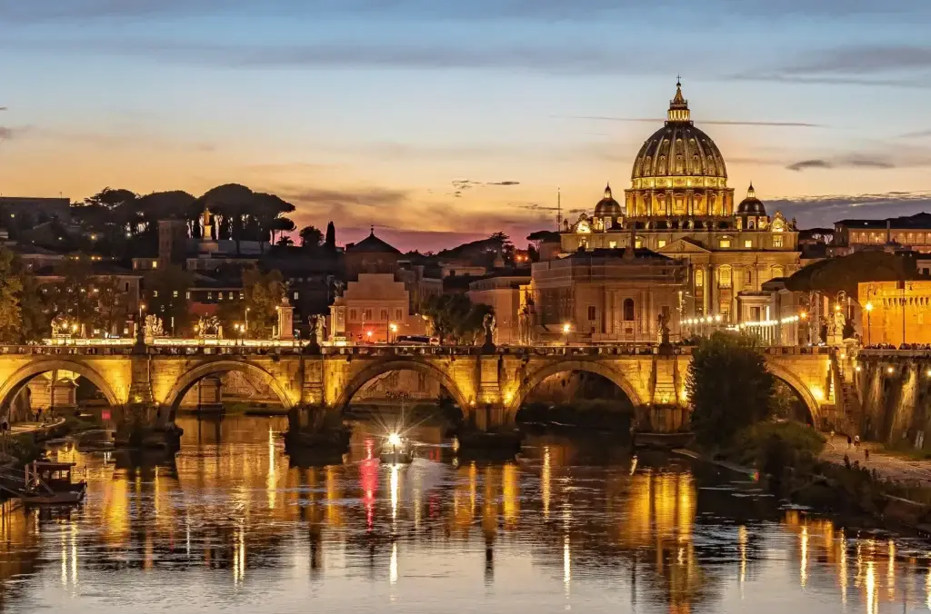 Stunning view of St. Peter's Basilica and Ponte Sant'Angelo at sunset in Rome, Italy, reflecting vibrant city lights and historic architecture on the Tiber River.