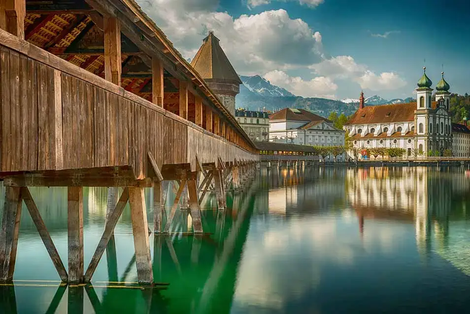 Chapel Bridge and Water Tower reflecting on the Reuss River in Lucerne, Switzerland with alpine mountains in the background