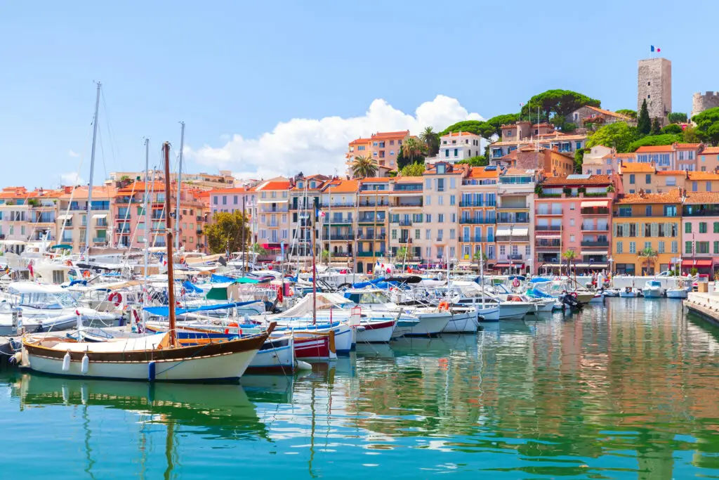 Colorful harbor with yachts and boats in the old port of Cannes, France, with pastel buildings and hillside views on the French Riviera