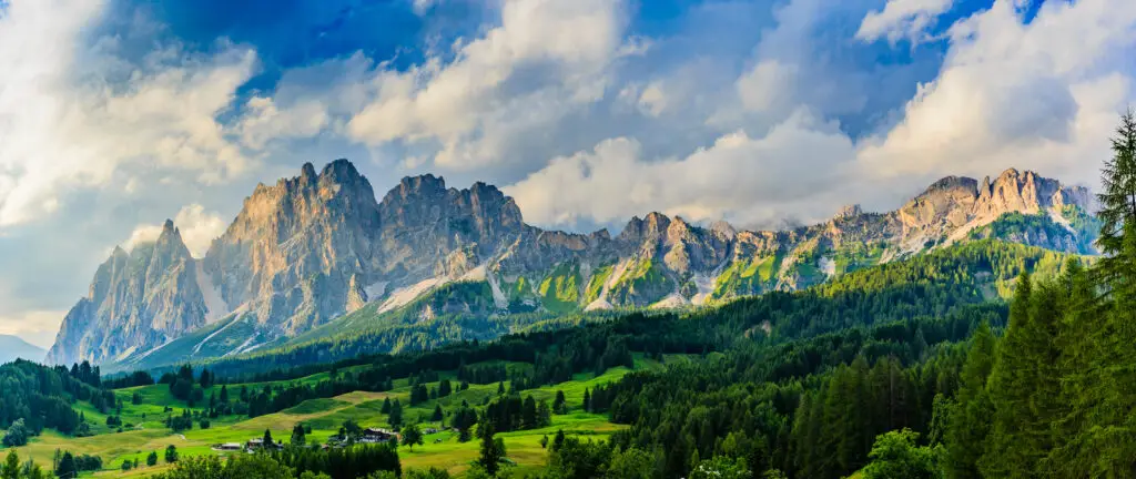 Scenic view of the Dolomites mountain range in northern Italy with lush green meadows, pine forests, and dramatic rocky peaks under a partly cloudy sky, a popular destination for Europe private tours and nature travel