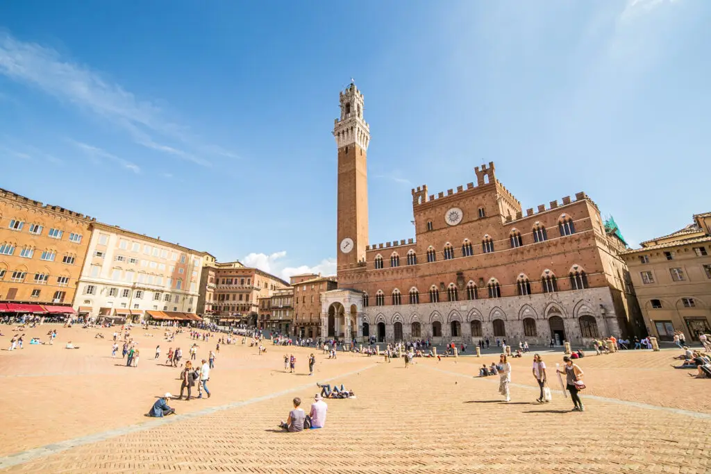 Piazza del Campo in Siena Italy with Torre del Mangia and Palazzo Pubblico surrounded by tourists enjoying the historic square on a sunny day
