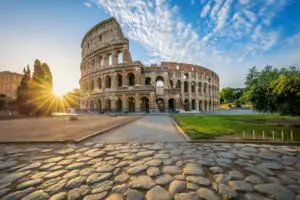 Colosseum in Rome Italy at sunrise with ancient stone pathway and beautiful blue sky, a famous historical landmark and popular tourist attraction in Europe