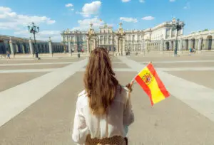 Tourist holding Spanish flag in front of the Royal Palace of Madrid, Spain during a sightseeing tour on a sunny day