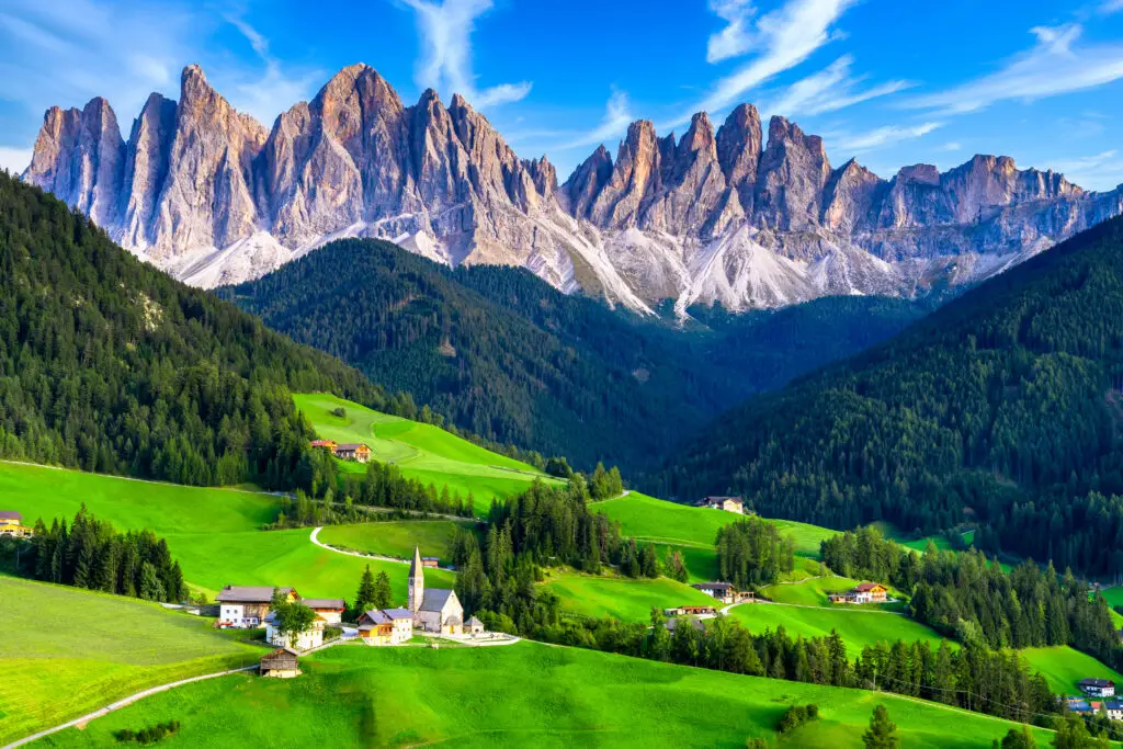 Scenic view of Santa Maddalena village in the Dolomites mountains, South Tyrol, Italy with green rolling hills, alpine meadows, and dramatic mountain peaks under a bright blue sky