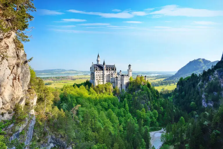 Neuschwanstein Castle surrounded by lush green forest and mountains in Bavaria, Germany, a popular European tourist attraction and fairytale castle destination