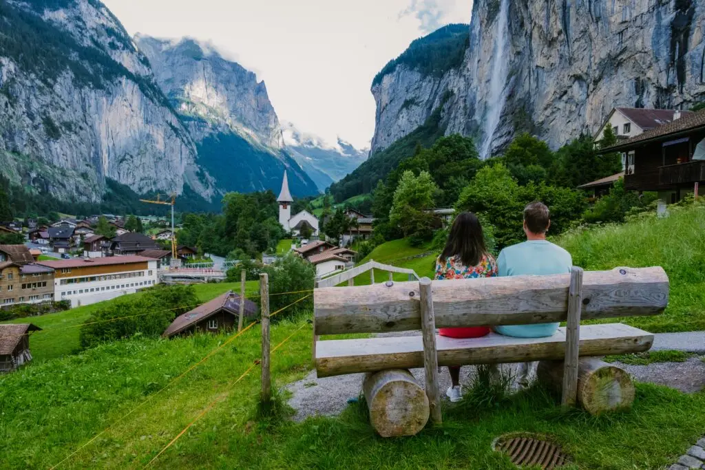 Couple enjoying scenic view of Lauterbrunnen Valley with waterfall, church, and alpine mountains in Switzerland
