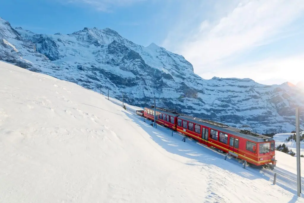 Scenic red train climbing through the snowy Jungfrau Region in Switzerland with stunning alpine mountain views in winter