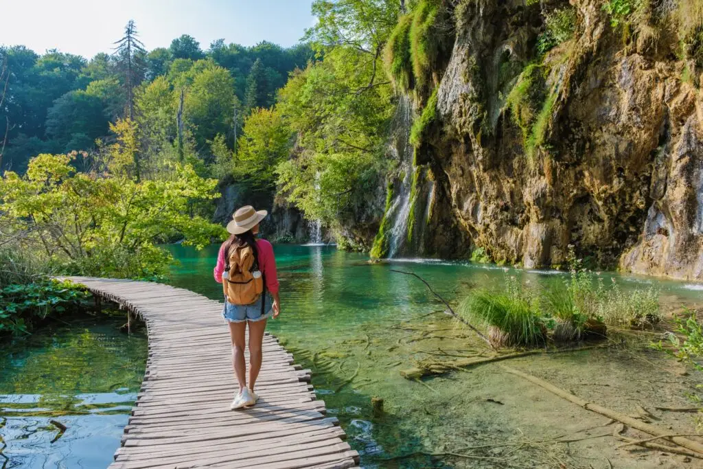 Traveler exploring wooden boardwalk along turquoise lakes and waterfalls at Plitvice Lakes National Park, Croatia