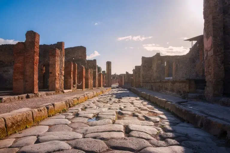 Ancient cobblestone street and ruins of Pompeii archaeological site in Italy under a sunny sky, showcasing historic Roman architecture and popular tourist attraction