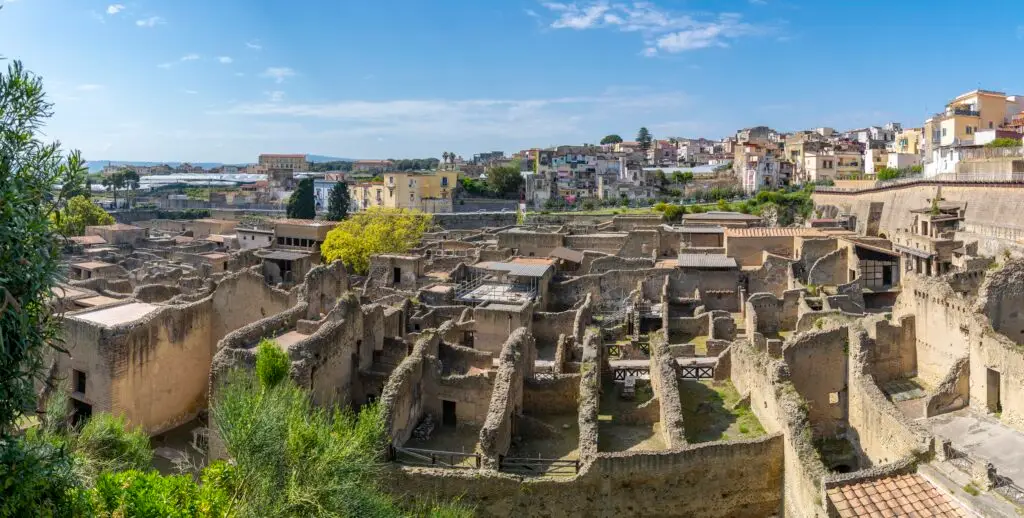 Ancient ruins of Herculaneum archaeological site in Campania Italy with preserved Roman buildings and cityscape in the background under a bright blue sky