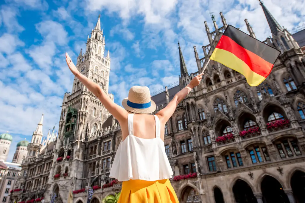 Tourist celebrating in front of the New Town Hall at Marienplatz in Munich Germany holding a German flag on a sunny day