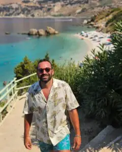 Graziano travel designer smiling by a turquoise beach on the Italian coast for private Italy tours