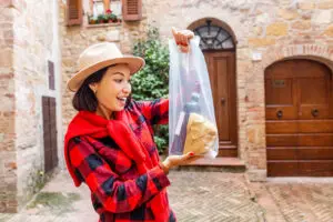 Happy Asian tourist shopping for Italian wine in a historic village street in Italy