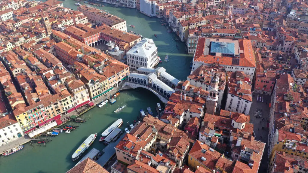 Aerial view of Rialto Bridge over the Grand Canal in Venice, Italy, with historic red-roofed buildings and boats