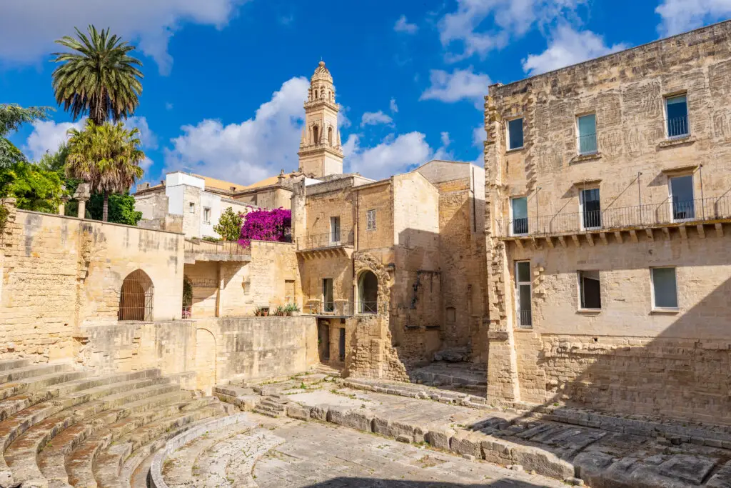 Bell tower of Duomo dell’Assunta in historic Lecce, Apulia, Italy, with ancient stone architecture and palm trees under a blue sky