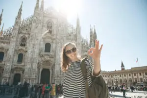 Smiling tourist with backpack at Milan Cathedral in Italy making an OK sign on a sunny private Italy tour