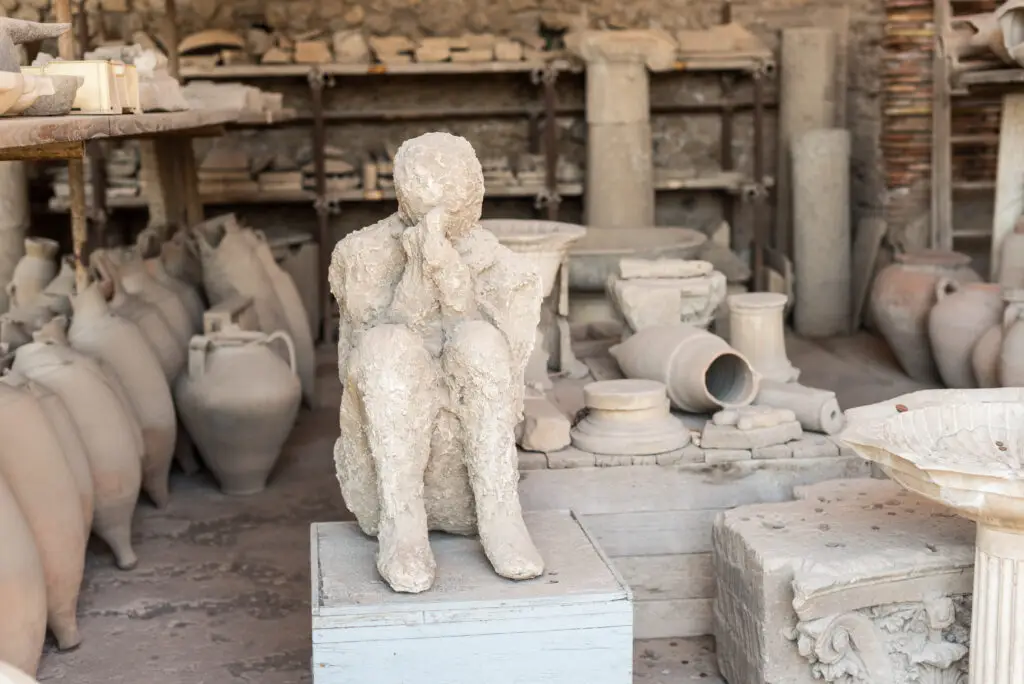 Plaster cast of a victim at the Roman archaeological site of Pompeii in Italy surrounded by ancient artifacts and amphorae