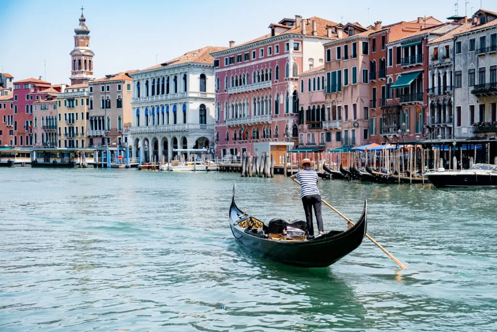 Gondolier rowing on the Grand Canal in Venice, Italy, with historic Venetian architecture in summer