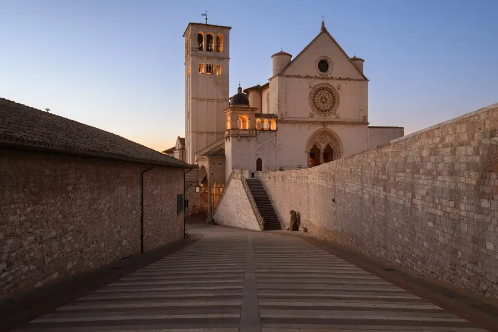 Basilica of Saint Francis of Assisi in Assisi, Italy, at sunset with medieval stone walkway and bell tower