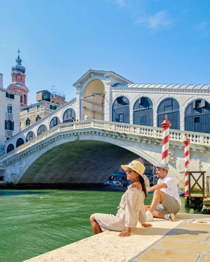 Couple of tourists enjoying a private Italy tour by the Rialto Bridge on the Grand Canal in Venice