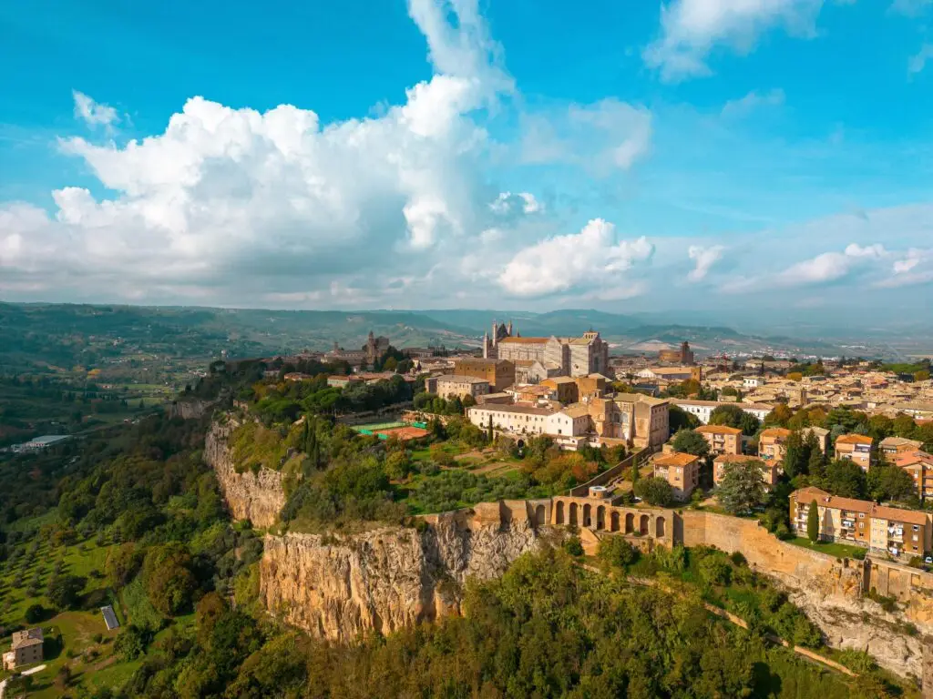 Aerial view of Orvieto, Italy with the Duomo cathedral, medieval hilltop town, cliffs, and Umbrian countryside under a blue sky
