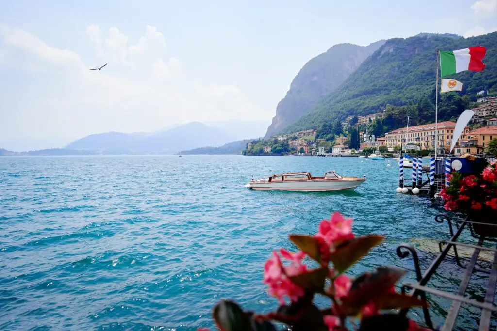 Lake Como waterfront in Menaggio, Lombardy, Italy with boat, Italian flag, mountains and village views