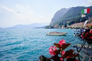 Lake Como waterfront in Menaggio, Lombardy, Italy with boat, Italian flag, mountains and village views