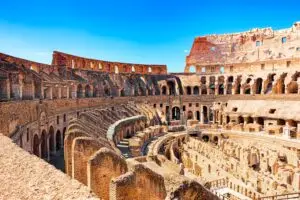 Interior ruins of the ancient Colosseum in Rome, Italy with historic arches and arena walls under a blue sky