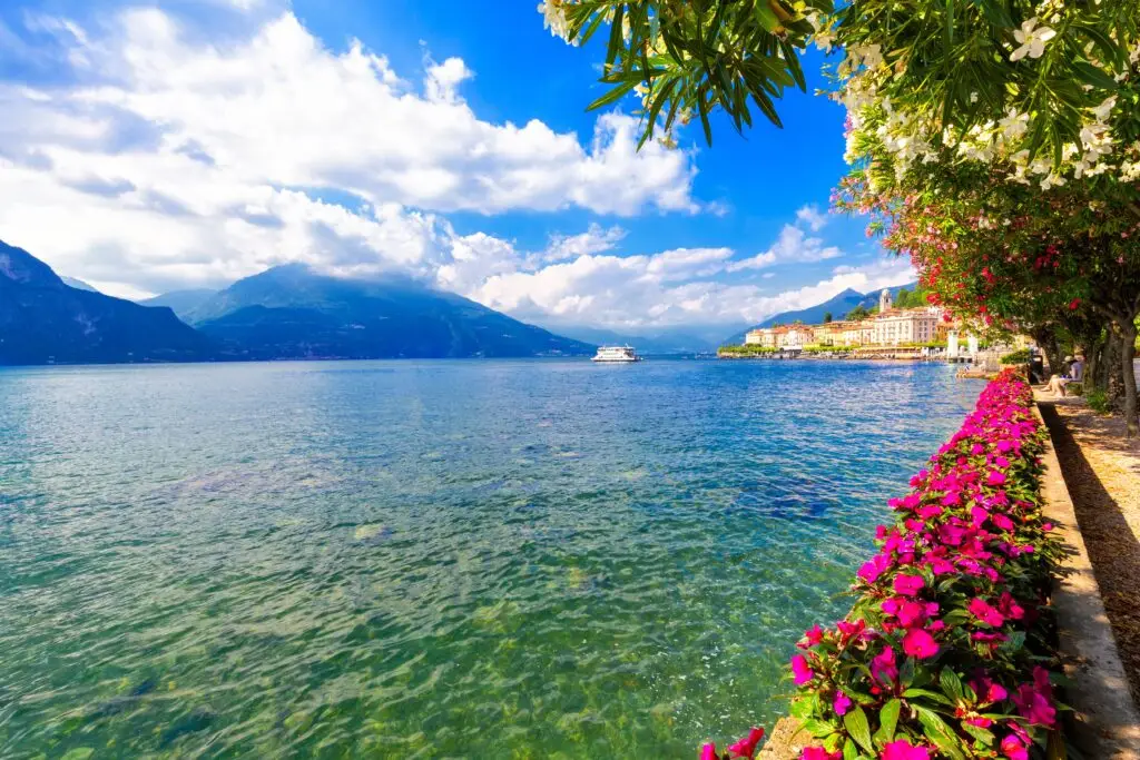 Flowers along the lakeside in Bellagio, Lake Como, Italy with mountain views and ferry on the water