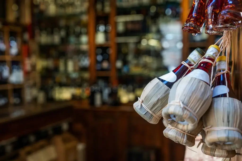Chianti red wine bottles in straw baskets displayed outside an Italian wine shop in Tuscany