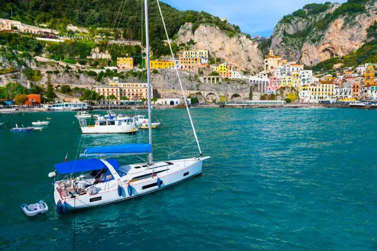 Sailboat in turquoise water with colorful Amalfi town and cliffs on the Amalfi Coast, Italy