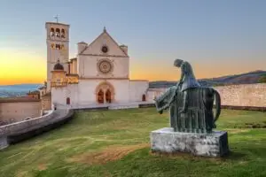 Basilica of Saint Francis of Assisi in Assisi, Italy at sunset with equestrian statue and Umbrian countryside view
