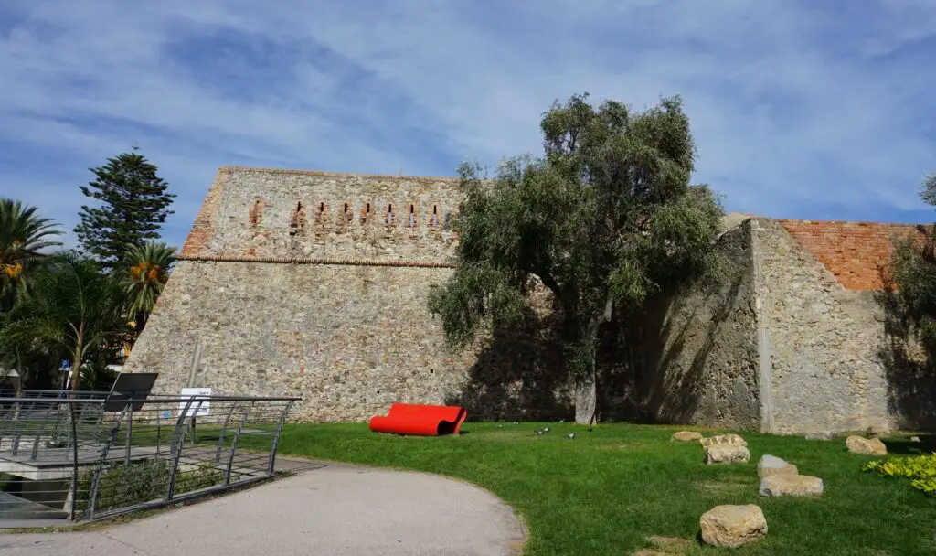 Exterior stone walls of the 18th century Forte di Santa Tecla in Sanremo, Italy with garden and olive tree