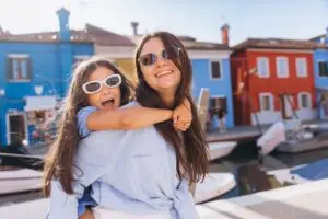Mother and daughter enjoying family travel in Burano, Venice, Italy with colorful houses and boats in the background