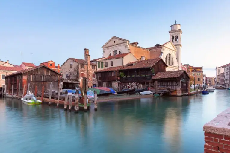 Traditional gondola workshop by a Venice canal with boats and a church tower in Italy
