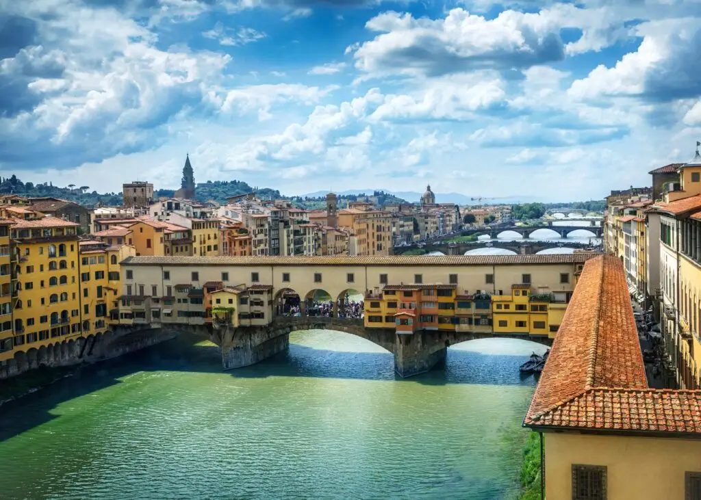 Ponte Vecchio Bridge spanning the Arno River in Florence, Italy, with historic city rooftops and Tuscan skyline