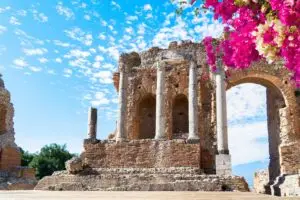 Ancient Greek Theatre of Taormina amphitheatre ruins in Sicily, Italy with bougainvillea and blue sky