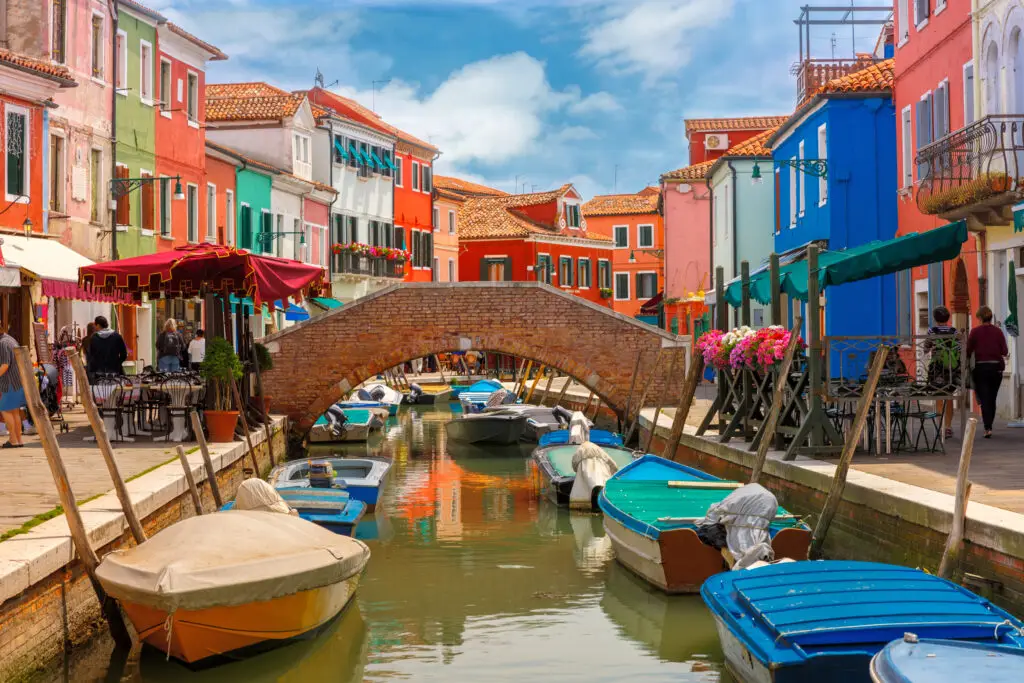 Colorful houses, boats, and brick bridge along a canal on Burano Island near Venice, Italy